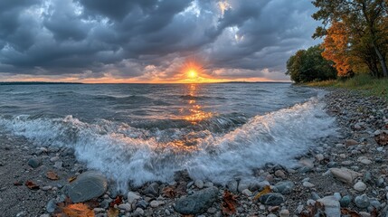 Dramatic sunset over lake with waves crashing on pebbled shore