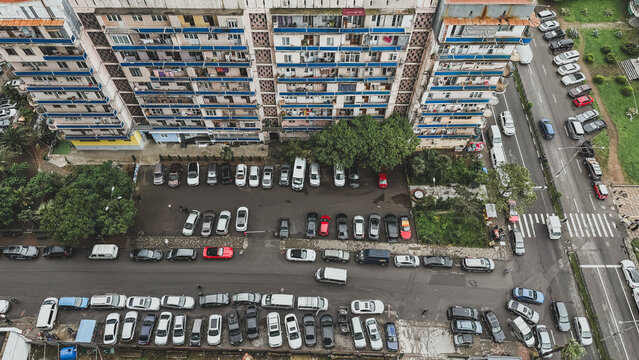 Aerial view of a Soviet-era apartment building and crowded parking lot in Batumi, Georgia, showing everyday urban life with tightly packed cars and residential balconies, concept of city life