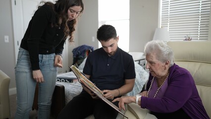 A warm family gathering occurs as grandmother reminisces with loved ones while flipping through a...