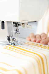 woman sews a light fabric on a sewing machine. making clothes, hobbies. a sewing studio, a clothing designer, a tailor sews on a household sewing machine.