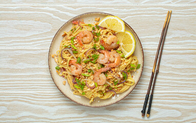 Pad thai noodles garnished with shrimp, peanuts, green onions, lemon wedges, and served with...
