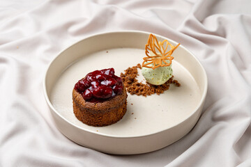 A beautifully arranged dessert features a cherry-topped cake beside a scoop of creamy ice cream, complemented by a delicate crunch. The presentation embodies elegance and indulgence