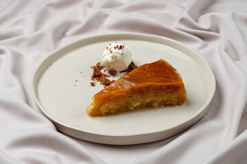 A luscious slice of caramelized dessert rests on a minimalist plate alongside a dollop of whipped cream, creating a perfect treat for a delightful afternoon