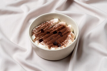 A delightful dessert features layers of creamy chocolate and soft whipped cream, garnished with dark chocolate pieces. The elegant presentation enhances its indulgent appeal on soft fabric