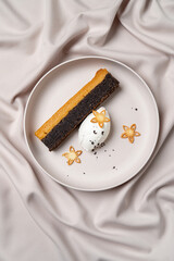 A beautiful dessert presentation features a layered sweet delicacy with a creamy ice cream scoop, adorned with delicate flower garnishes on a soft textile backdrop, perfect for an upscale gathering