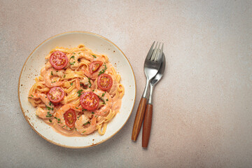 Seafood linguine pasta in creamy sauce with shrimp and cherry tomatoes, garnished with fresh parsley, served on a light warm beige background with cutlery top view, copy space