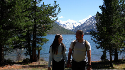 Mountain travel. A couple with backpacks reached a mountain lake, snowy peaks in the distance....