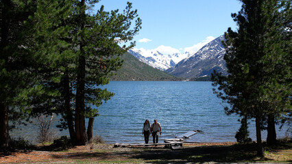 Mountain travel. A couple with backpacks reached a mountain lake, snowy peaks in the distance....