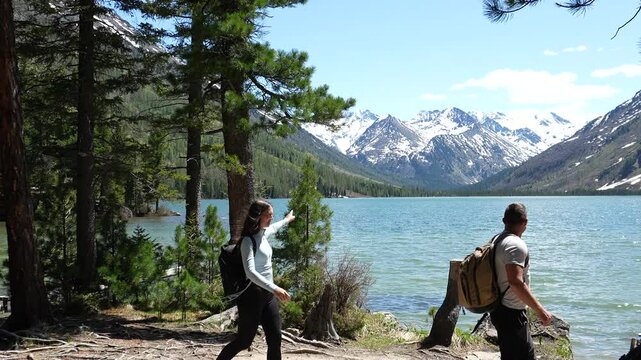 Mountain Travel. A couple with backpacks reached a mountain lake, snowy peaks in the distance. Mountain Travel and Hiking