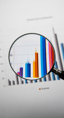 Magnifying glass focuses on bar chart detail, showcasing business growth analysis, representing data examination and strategic planning for improved market understanding