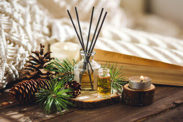 Assortment of natural Christmas essential oils in small bottles. Candles, branches of fir tree, home aroma diffuser. Aromatherapy, cozy atmosphere, holiday festive mood. Close up macro, wooden table