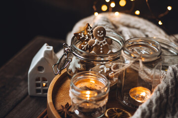 Big glass jar with homemade gingerbread cookies for Santa Claus. Idea for handmade present, gift for family and friends. Cozy atmosphere, simple festive home decor with candles, fairy lights