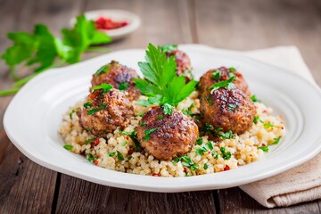 Juicy meatballs are artistically arranged atop a flavorful couscous base, garnished with fresh herbs. The wooden table enhances the inviting atmosphere of a homemade meal