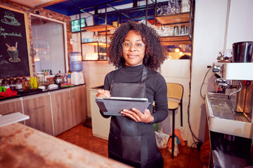 Confident black female barista using digital tablet in coffee shop