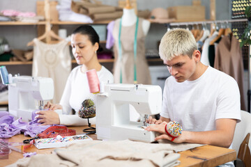 Tailors are working on a collection of clothes. Male tailor working in team with Asian female...