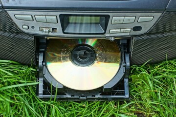 one round shiny yellow compact disc music with information inserted into black disc drive of old plastic stereo tape recorder with buttons on green grass