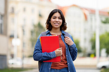 Outdoor portrait of smiling arab female student with backpack and workbooks, happy young middle...