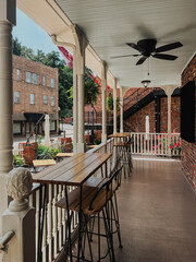 Charming vintage balcony with wood tables, black stools, ceiling fan, hanging ferns, ornate...