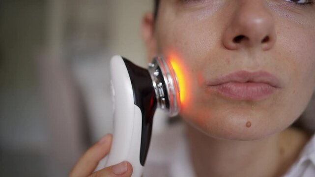 Woman using EMS lifting and LED light therapy device for facial contouring and skincare