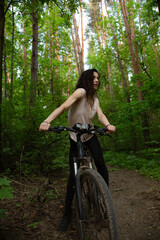 Beauty smiling woman biking on bicycle on spring trees green forest background, looking happy around. Enjoying fun girl outdoors. Female riding in park in sport clothes. Full lenght portrait