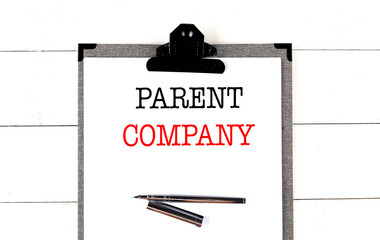 Parent company phrase on clipboard with pen on white wooden desk background