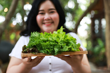 A smiling plus-size woman holding a wooden tray filled with fresh leafy greens,healthy living and natural food
