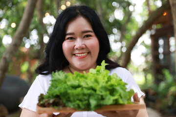 A smiling plus-size woman holding a wooden tray filled with fresh leafy greens,healthy living and natural food