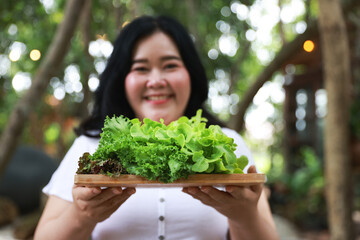 A cheerful plus-size woman holding a wooden tray filled with fresh green lettuce, symbolizing healthy eating and a balanced lifestyle