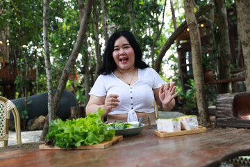 A cheerful plus-size woman holding a wooden tray filled with fresh green lettuce, symbolizing healthy eating and a balanced lifestyle