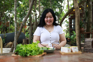A cheerful plus-size woman holding a wooden tray filled with fresh green lettuce, symbolizing healthy eating and a balanced lifestyle