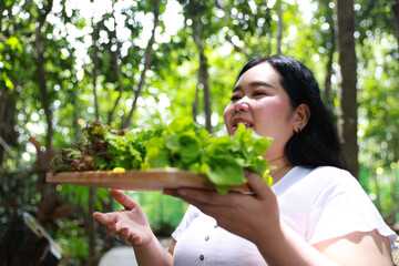 A smiling plus-size woman holding a wooden tray filled with fresh leafy greens,healthy living and natural food
