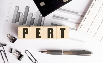 PERT word on wooden blocks with charts, calculator, pen, binder clips and credit card on white office desk