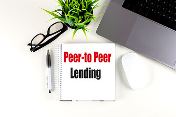 Peer-to-peer lending text on spiral notebook with laptop, glasses, pen, mouse and plant on white desk