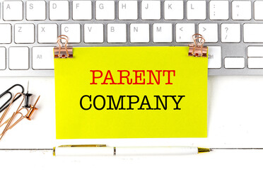 Parent company text on yellow paper sheet pinned on keyboard with pen and office supplies
