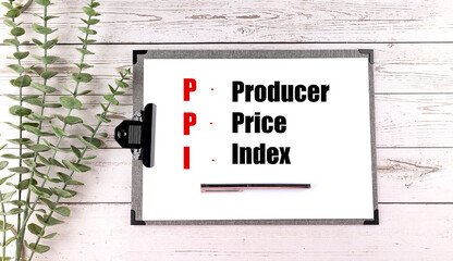 PPI producer price index abbreviation on clipboard with pen and eucalyptus on white wooden background