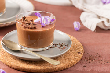 A delicious chocolate mousse dessert in a glass, beautifully presented with purple flowers and chocolate shavings, styled for an inviting look.