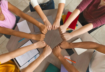 Multiracial students joining hands together, preparing common academic project, top view