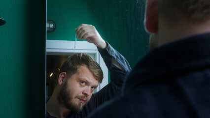 Bearded man raises a key above his head while looking in the mirror, creating a mysterious or...