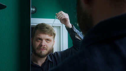 Bearded man looks intensely at his reflection while holding a key above his head, suggesting introspection or symbolic gesture.