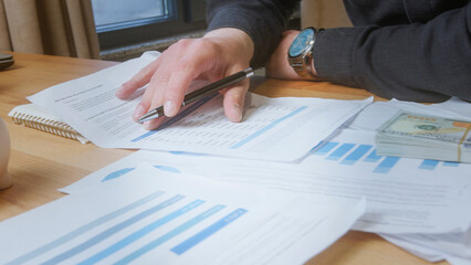 Person's hand holding a pen points at printed charts and graphs, indicating financial analysis, business planning, or data review.