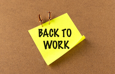 Back to work message on yellow sticky note pinned to corkboard with pushpins as motivational reminder