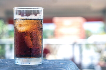 Glass of refreshing cola with ice on table