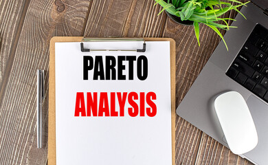 Pareto analysis text on clipboard with laptop, white mouse, silver pen and plant on wooden desk
