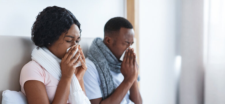 African american man and woman got cold, sneezing their noses, staying in bed during illness, copy space. Black couple with scarfs around their necks having flue. Cold and flue concept