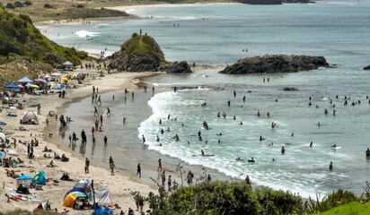 Families and friends spend a sunny summer day relaxing under tents and umbrellas on a busy beach in Tawharanui, Warkworth, Auckland, New Zealand