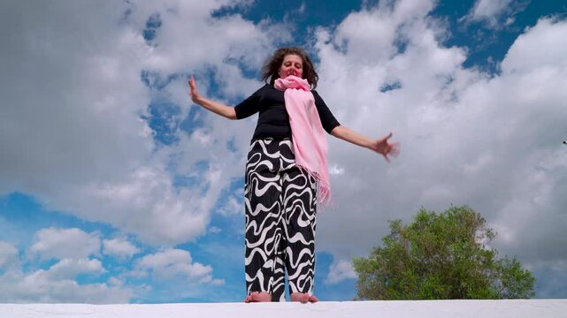 Mujer corriente haciendo equilibrio para poder llegar a fin de mes, un d&iacute;a soleado con cielo azul y nubes.