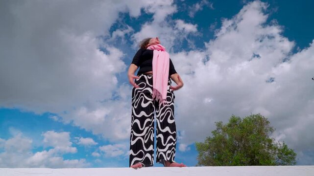 Mujer corriente haciendo ejercicios de equilibrio y coordinaci&oacute;n un d&iacute;a soleado con cielo azul y nubes.