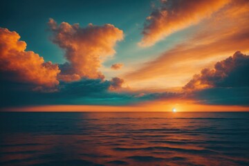 A breathtaking sunset over the ocean paints the sky with dramatic hues of orange, blue, and teal, with clouds reflecting the vibrant, golden light.
