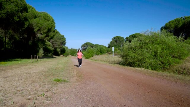 Mujer corriente corriendo por el bosque un d&iacute;a soleado con cielo azul.