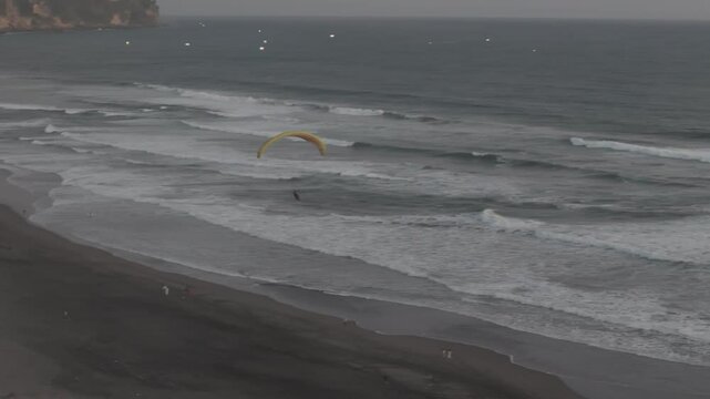  powered paraglider (paramotor) flying low above the ocean waves during sunset near a tropical beach in Indonesia. The calm sea and golden sky create a serene and adventurous atmosphere.